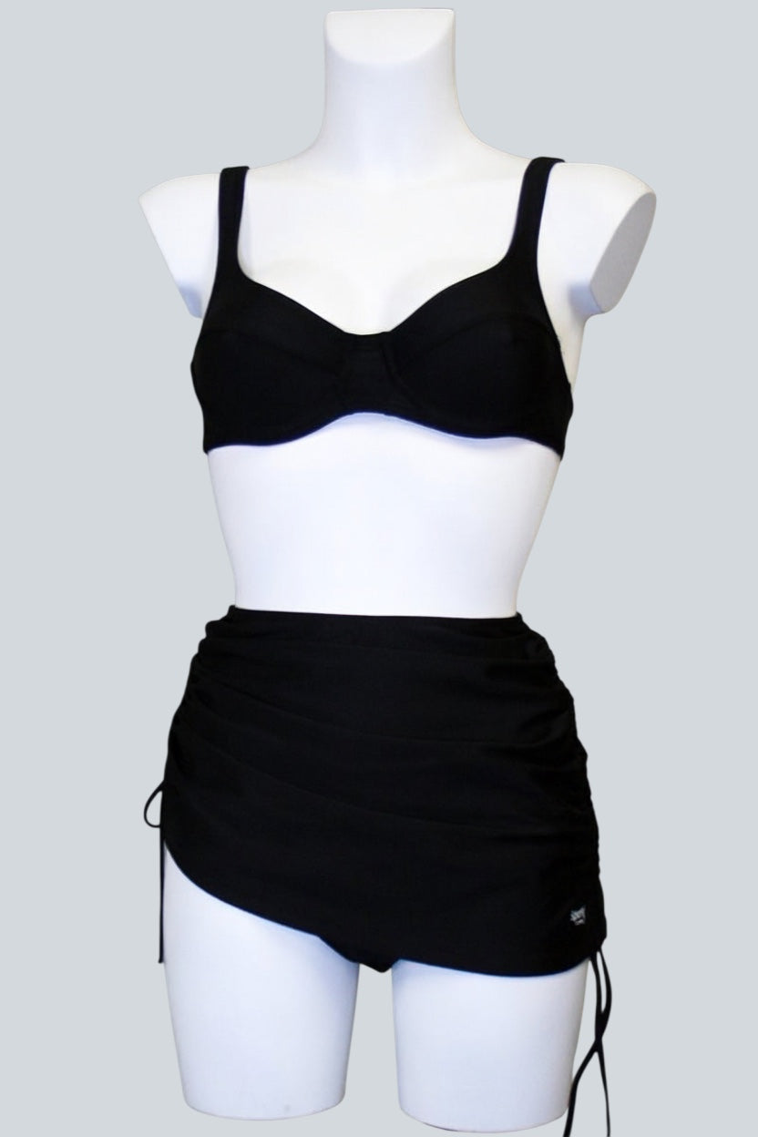 Care Design Athen black bikini bottoms with skirt for women with stoma, featuring a discreet inner pocket and adjustable side ties.
